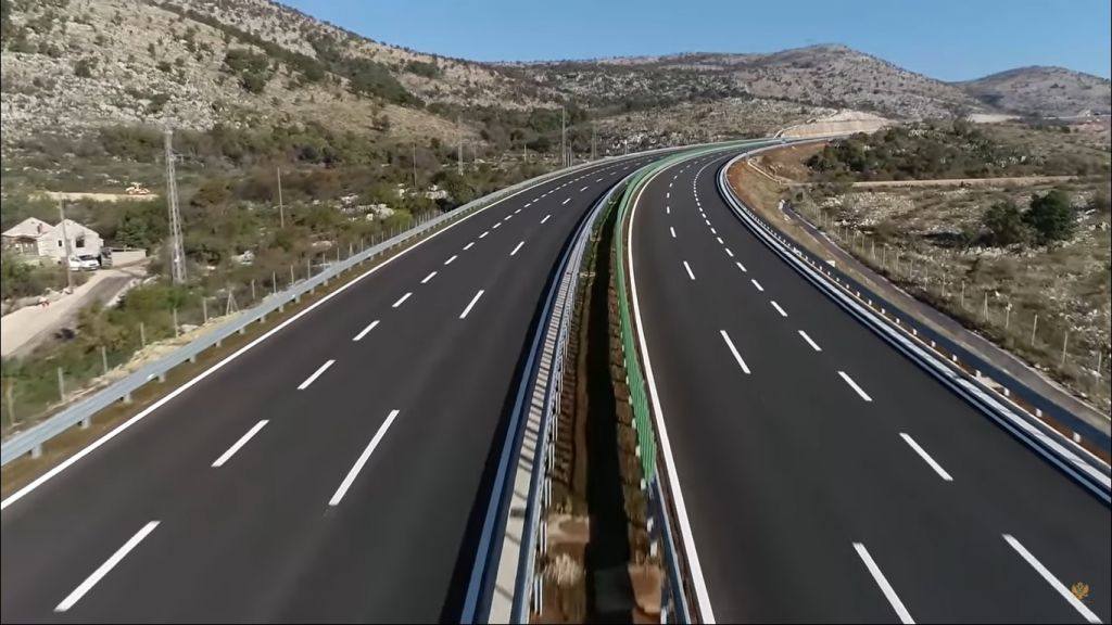 Kraj saobraćajnim čepovima: Kako će nova dionica spojiti Nikšić, Cetinje i jug bez ulaska u grad Iako je dugačka svega oko tri kilometra, Zapadna obilaznica predstavlja ključnu sponu u saobraćajnoj mreži Podgorice čiji značaj daleko prevazilazi njenu dužinu. Nova saobraćajnica povezaće kružni tok kod salona namještaja „Grand“ u Donjoj Gorici sa kružnim tokom na Komanskom mostu, čime će se spojiti pravci prema Nikšiću, Cetinju i jugu države i rasteretiti gradsko jezgro. Projektom je predviđeno da trasa bude izgrađena kao bulevar sa četiri saobraćajne trake, trotoarima sa obje strane i savremenom javnom rasvjetom. Kod Komanskog mosta izlaziće koridor prema Danilovgradu i Nikšiću. Time vozila koja putuju između sjevera i primorja ili aerodroma više neće morati da prolaze kroz opterećene gradske saobraćajnice. Olakšanje za Zabjelo i Bulevar Vojislavljevića Najveće direktne koristi od ovog projekta trebalo bi da osjete stanovnici Zabjela i naselja duž Bulevara Vojislavljevića. Cilj je da se dio tranzitnog, a posebno teretnog saobraćaja preusmjeri na novu obilaznicu, čime će kamioni čije krajnje odredište nije Podgorica biti izmješteni iz gusto naseljenih zona. Rok za završetak radova je 550 kalendarskih dana, a on počinje zvaničnim uvođenjem izvođača u posao, čiji se početak gradnje očekuje do kraja ove godine.